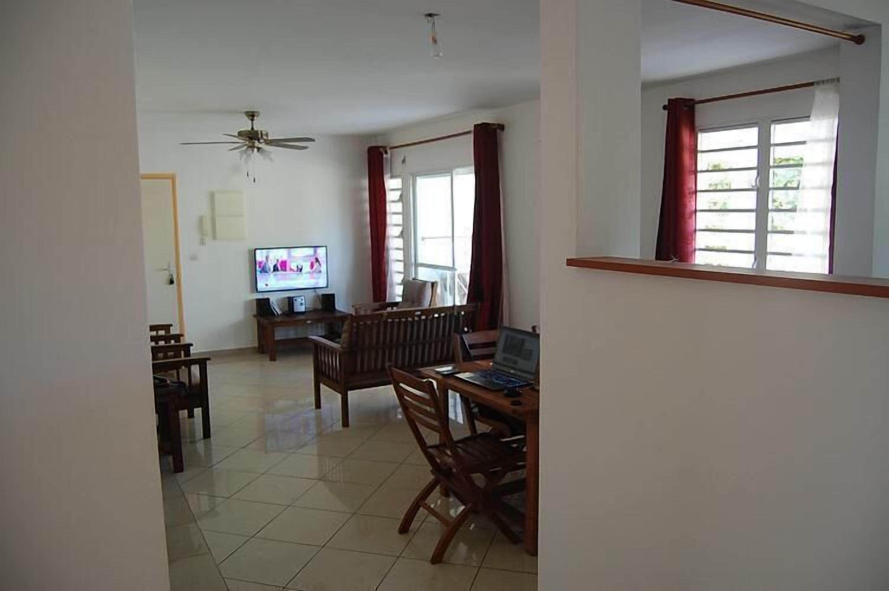 A living room with a TV, wooden furniture, a ceiling fan, and a window with curtains.