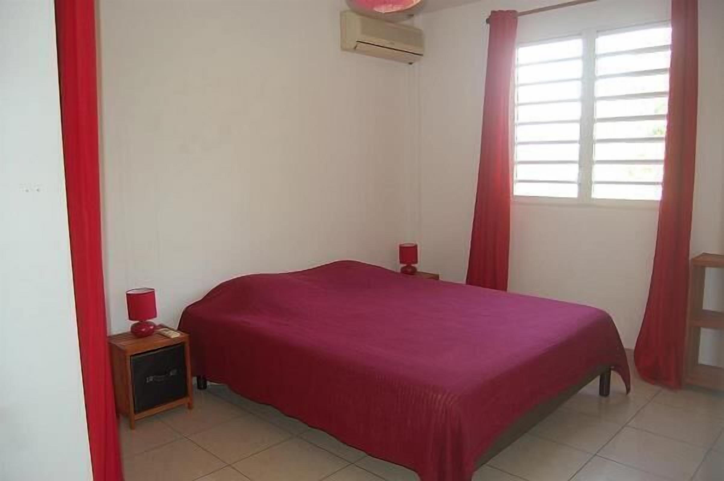 A bedroom with a bed, a nightstand, a lamp, and a window with curtains.