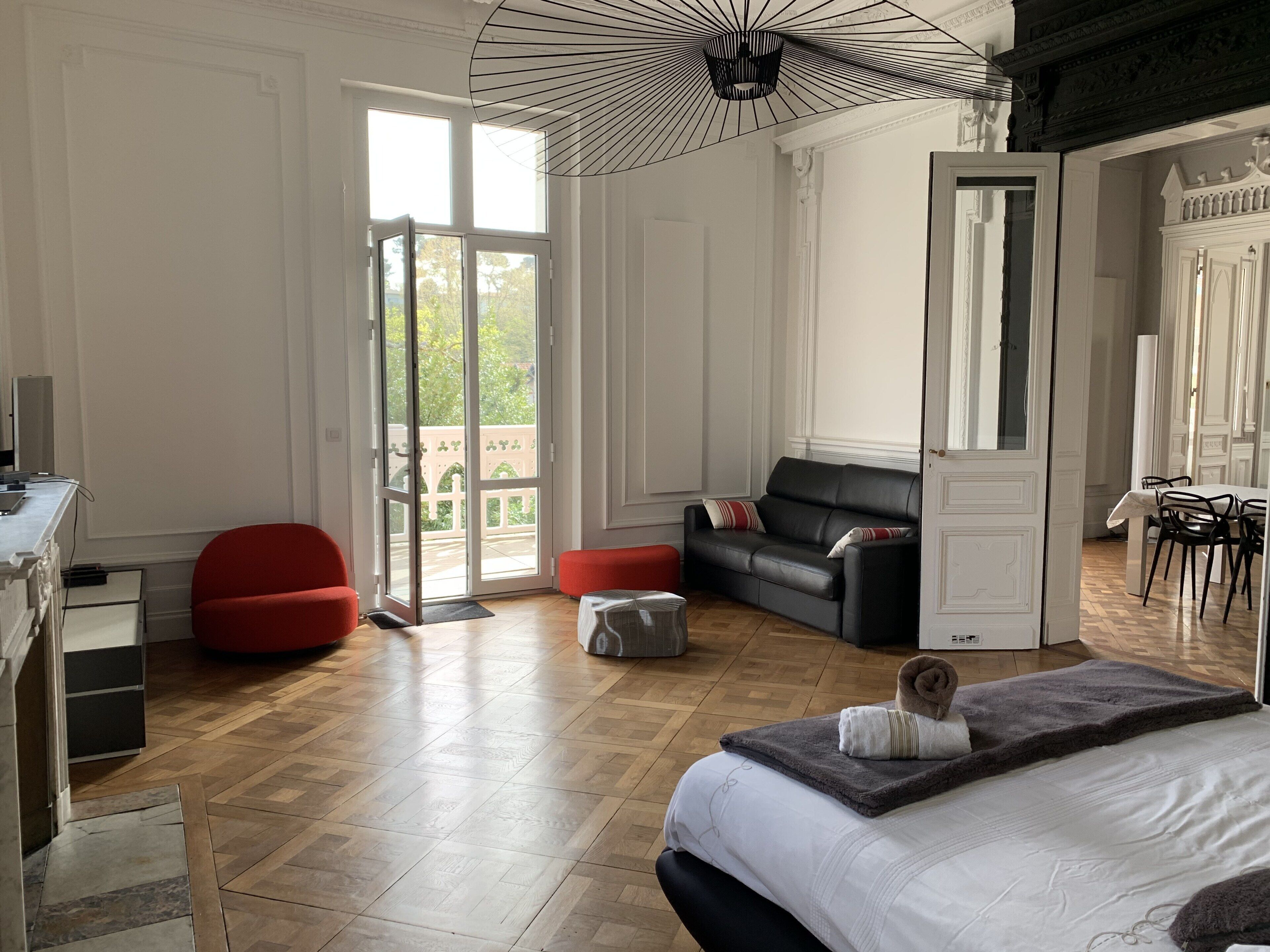 Un dormitorio moderno con una cama grande, una silla roja, un sofá negro y una zona de comedor con una mesa y sillas.