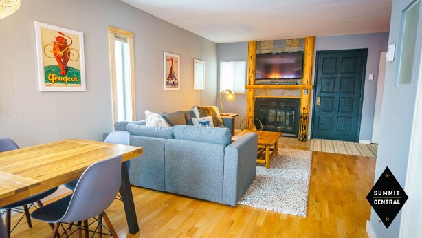 A cozy living room with a grey sofa, wooden dining table, and a fireplace. - Cozy, modern 2BD/2BA townhome minutes from 4 world class ski resorts. (Silverthorne)