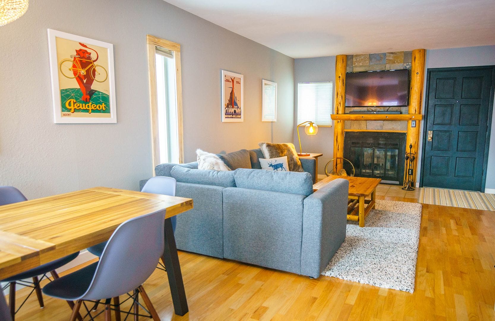 A cozy living room with a grey sofa, wooden dining table, and a fireplace.