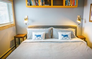 A bedroom with a bed, two pillows with animal prints, bedside lamps, a bookshelf, and a framed map on the wall.