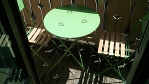 Una mesa metálica verde con un banco de madera, frente a una cerca de metal.