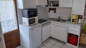 Una cocina compacta con armarios blancos, microondas, refrigerador pequeño, pileta y cafetera.