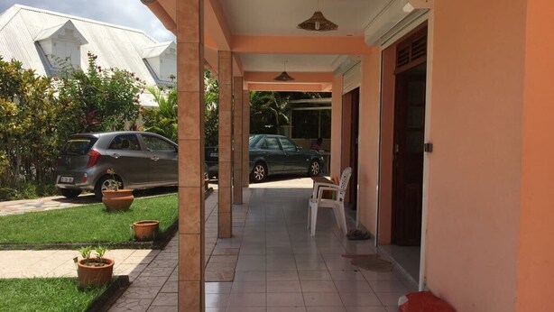 A covered outdoor area with a tiled floor, a white chair, and a car parked in the background. - Nice apartment perfect also for people with reduced mobility (Sainte-Anne)