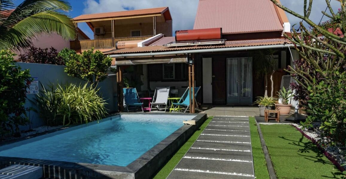 A swimming pool with lounge chairs, a covered patio, and a house with a red roof.