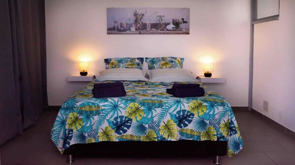 Un lit recouvert d’une couvre-lit à motifs floraux, deux lampes de chevet et un tableau accroché au mur.
