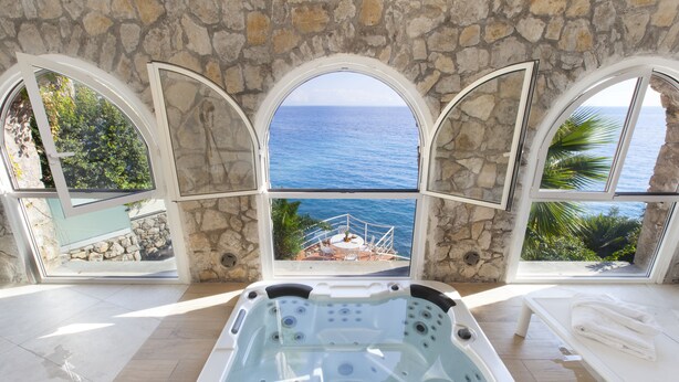 Ein Wellnessbereich mit Whirlpool, Steinwänden und Meerblick.