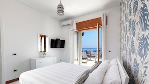 Ein Schlafzimmer mit einem großen Bett, einem Fernseher, einem Schminktisch und Meerblick durch eine offene Tür.