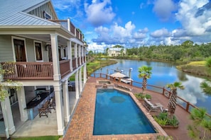 A two-story building with a pool, a dock, and a view of a river. - Waterfront Retreat • Outdoor Bar + Pool | Dock | Bay Views (Pass Christian)