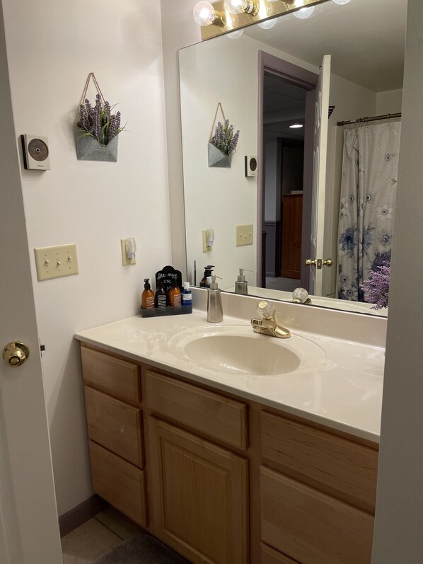 Une salle de bain avec un grand miroir, un lavabo blanc, des meubles en bois et un rideau de douche.
