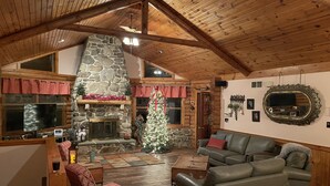A cozy cabin interior with a stone fireplace, a Christmas tree, leather sofas, and a wooden ceiling. - Working Horse Ranch With Indoor Pool!! (Grantville)