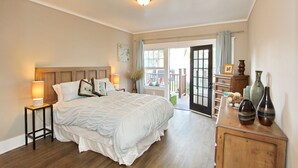 A bedroom with a bed, bedside lamps, a dresser with vases, and a view of the outdoors through a door.