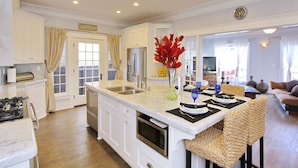 A spacious kitchen with white cabinetry, a large island with bar stools, a built-in oven, and a dining area with a table set for four.