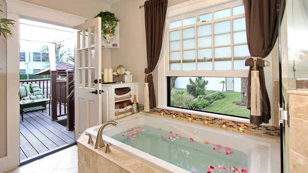 A bathroom with a bathtub, a window with a view of greenery, and a door leading to a deck.