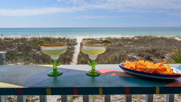Two margarita glasses on a colorful table with a beach view in the background. - One NITE  MINIMUM  5 steps off deck onto beach; 10 steps out front door to pool. (Panama City Beach)