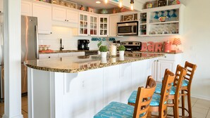 A kitchen with white cabinets, a granite countertop, and a bar area. - One NITE  MINIMUM  5 steps off deck onto beach; 10 steps out front door to pool. (Panama City Beach)