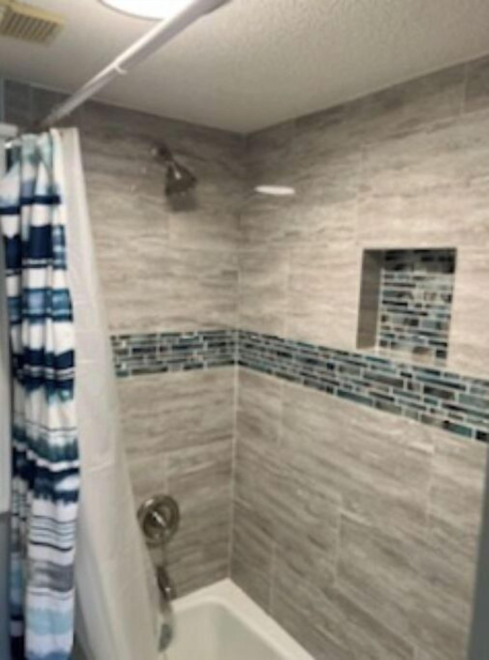 Un baño con ducha, paredes de azulejos y una cortina.
