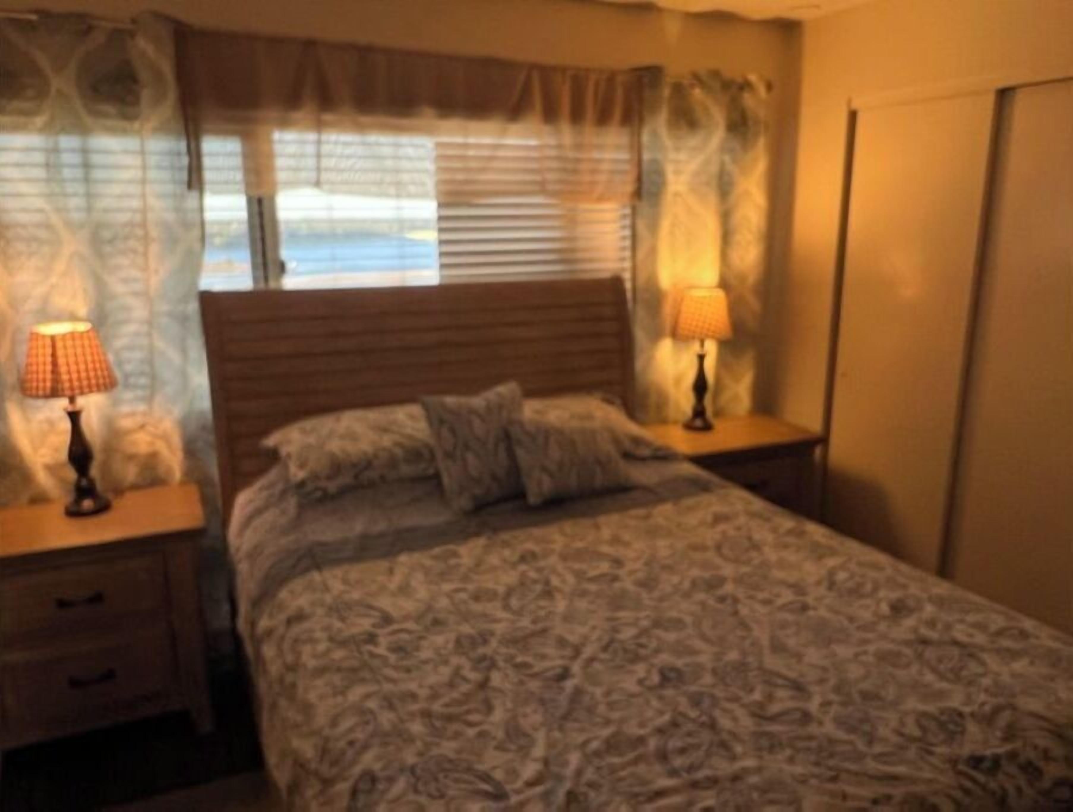 Une chambre à coucher avec un lit, deux tables de chevet avec des lampes, une fenêtre avec des stores et une porte.