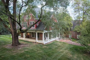 Een rode bakstenen woning met een witte veranda en een grote boom op de voorgrond.