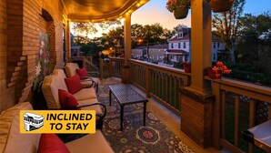 A covered porch with seating, hanging flower baskets, and a view of the neighborhood. - Family-Focused Victorian In Quiet Area, Pets OK, Yard & Parking (Pittsburgh)