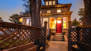 A two-story house with a red door, a staircase leading to the entrance, and a wooden fence in the foreground. - Family-Focused Victorian In Quiet Area, Pets OK, Yard & Parking (Pittsburgh)