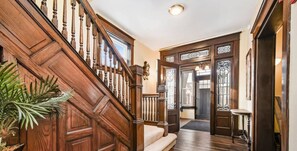 Una escalera de madera que lleva a una puerta con panel de vidrio, un banco y una planta en maceta.