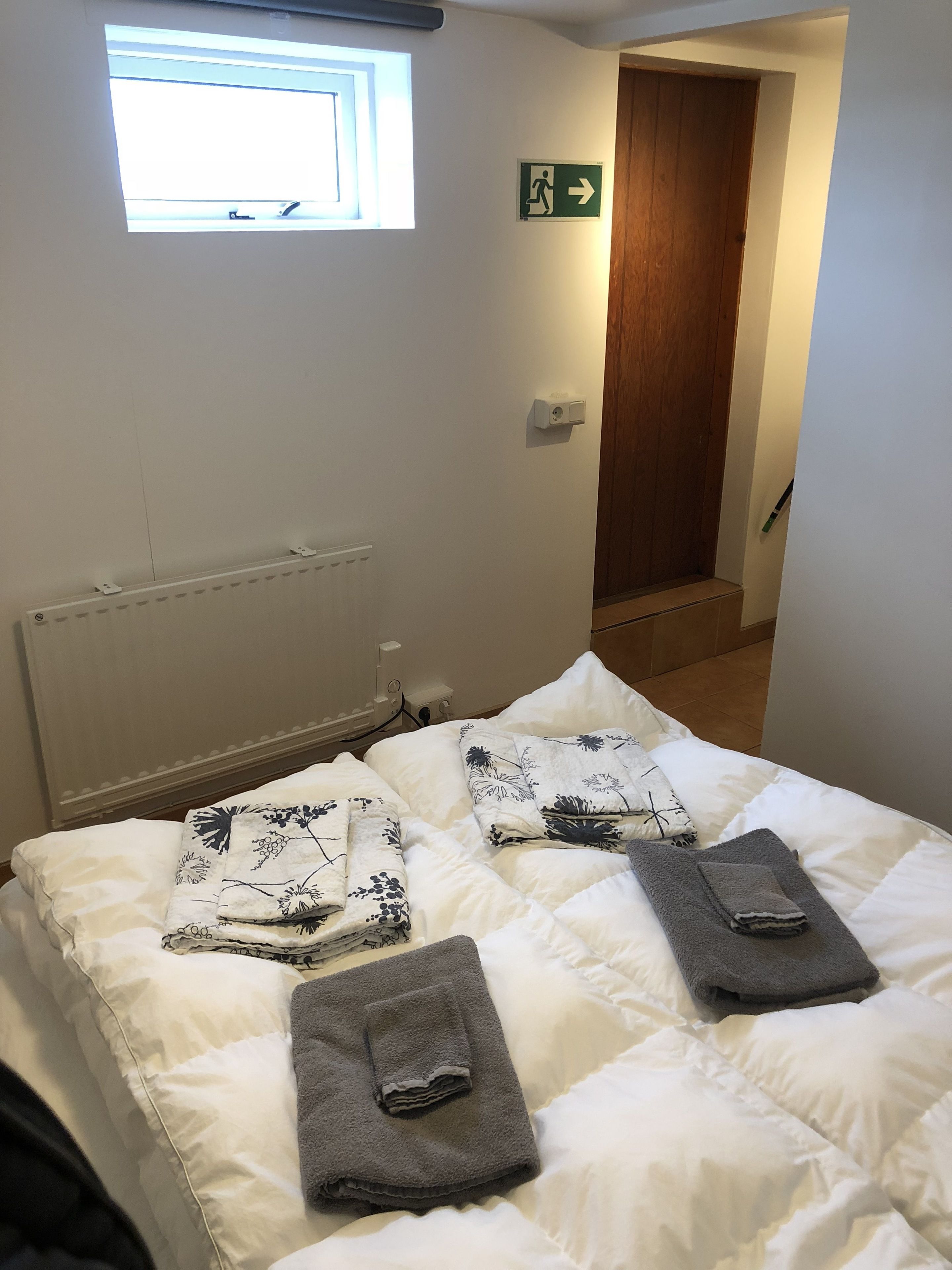 A hotel room with a bed, a window, a door, and a wall-mounted light switch.