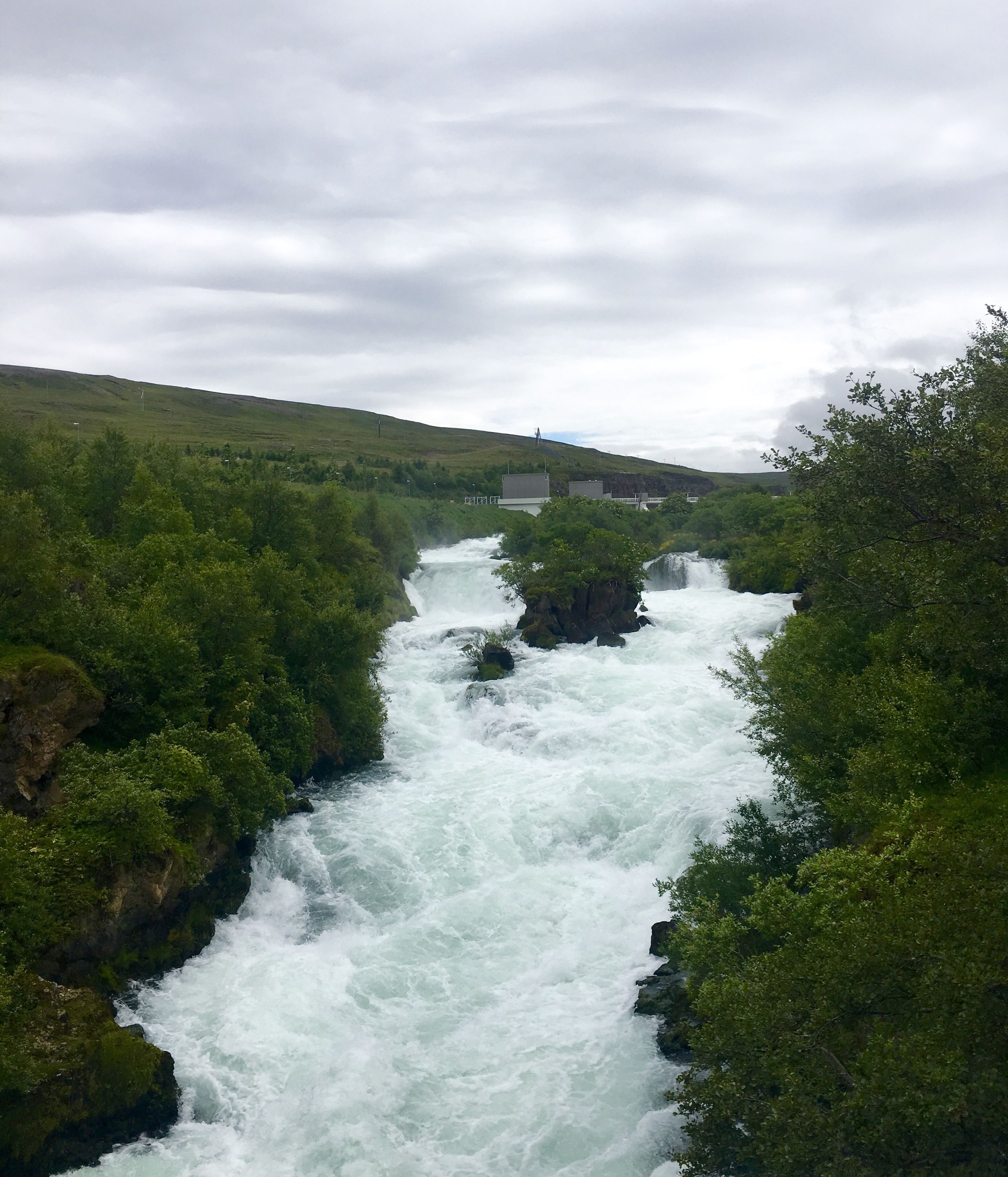 Une rivière traverse un paysage verdoyant et luxuriant, avec un barrage en arrière-plan.