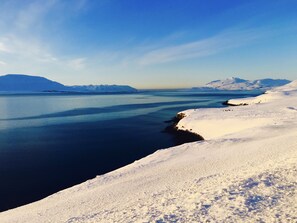 A panoramic view of a snowy landscape with a calm body of water and distant mountains.