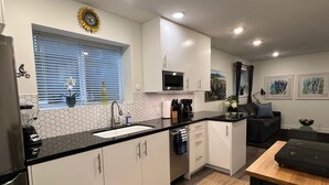 Una cocina moderna con armarios blancos, encimera negra, microondas integrado y una ventana con persianas.