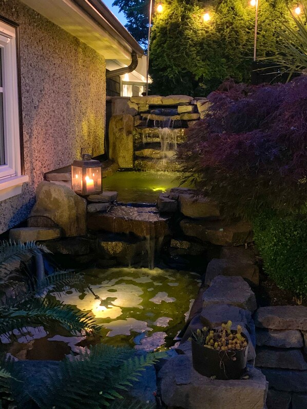 A stone waterfall feature with a small pond, surrounded by rocks and plants. - Kitsilano Oasis: Quiet and Spotlessly Clean Garden Suite with King Bed ★ ★ ★ ★ ★ (Vancouver)