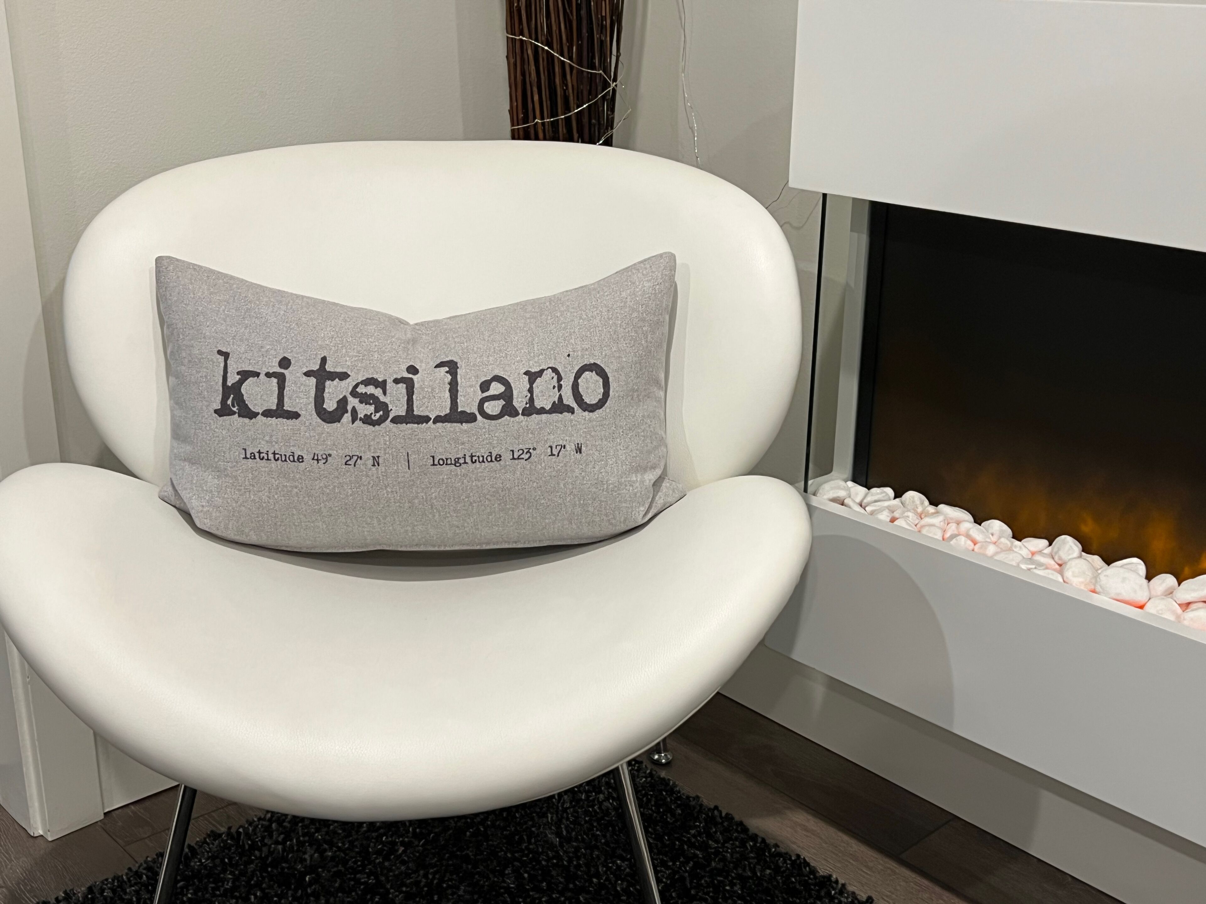 Valkoinen tuoli, jossa on tyyny, jossa lukee teksti »kitsilano» ja jossa on koordinaatit.
