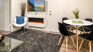 Una sala moderna con chimenea, un televisor montado encima, un comedor con una mesa redonda y sillas, y una planta decorativa.