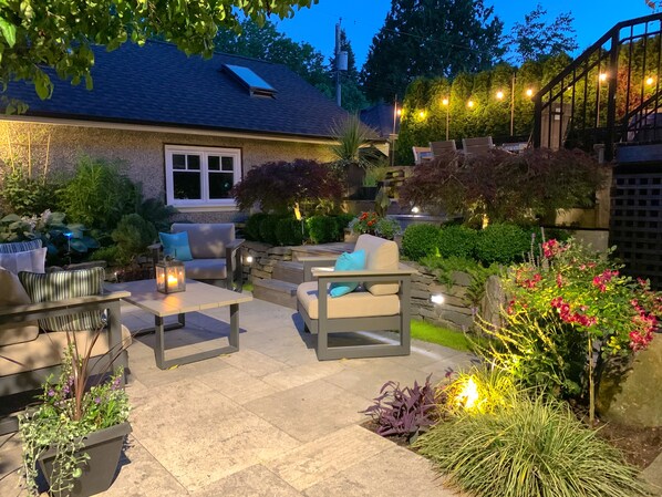 Eine Außenpatio-Terrasse mit Steinböden, einer Sofagarnitur und verschiedenen Kübelpflanzen.
