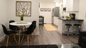 Una cocina moderna con armarios blancos, encimera negra y electrodomésticos de acero inoxidable. Cuenta con un comedor con una mesa redonda y sillas negras.