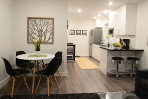 Una cocina moderna con armarios blancos, encimera negra y electrodomésticos de acero inoxidable. Cuenta con un comedor con una mesa redonda y sillas negras.