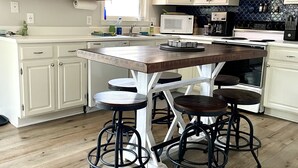 Una cocina con armarios blancos, una isla de madera con taburetes, un microondas y una cafetera.
