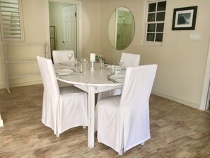 A dining area with a round table set for four, white chairs, and a mirror on the wall.