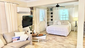 Et godt oplyst rum med sofa, fladskærms-TV, seng og loftventilator.