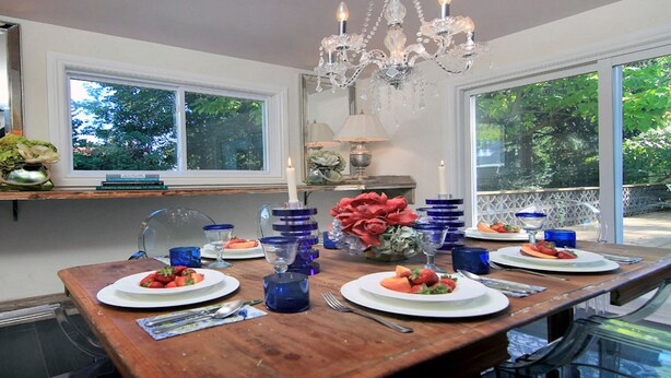 Un coin repas avec une table en bois dressée pour quatre personnes, entourée de grandes fenêtres donnant sur un paysage verdoyant.