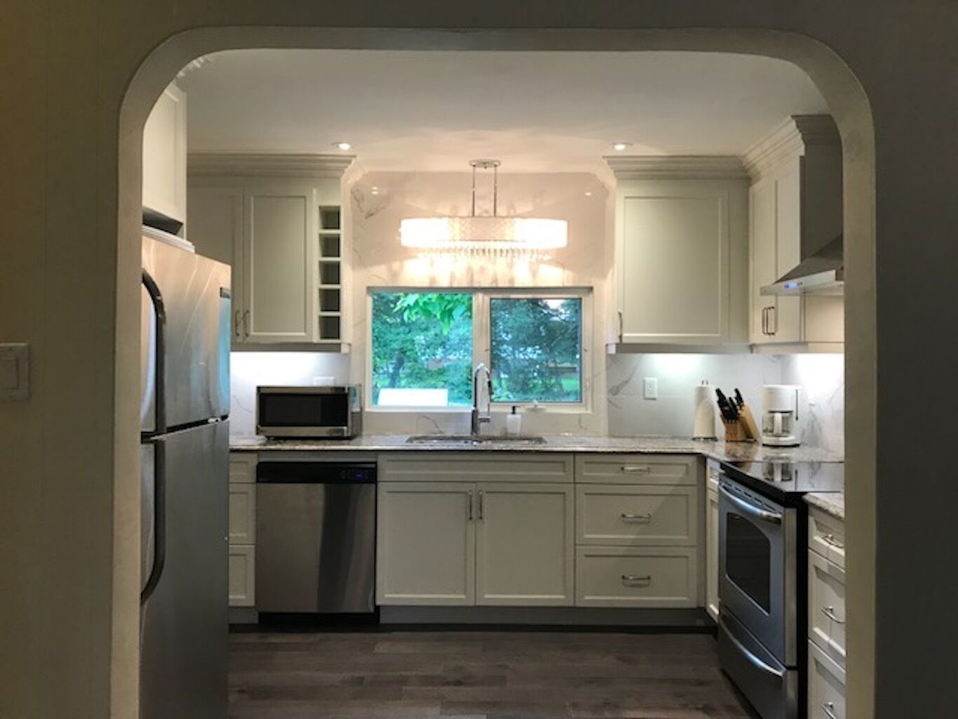 Una cocina moderna con armarios blancos, un refrigerador de acero inoxidable, un microondas, un lavavajillas, un fregadero y un horno.
