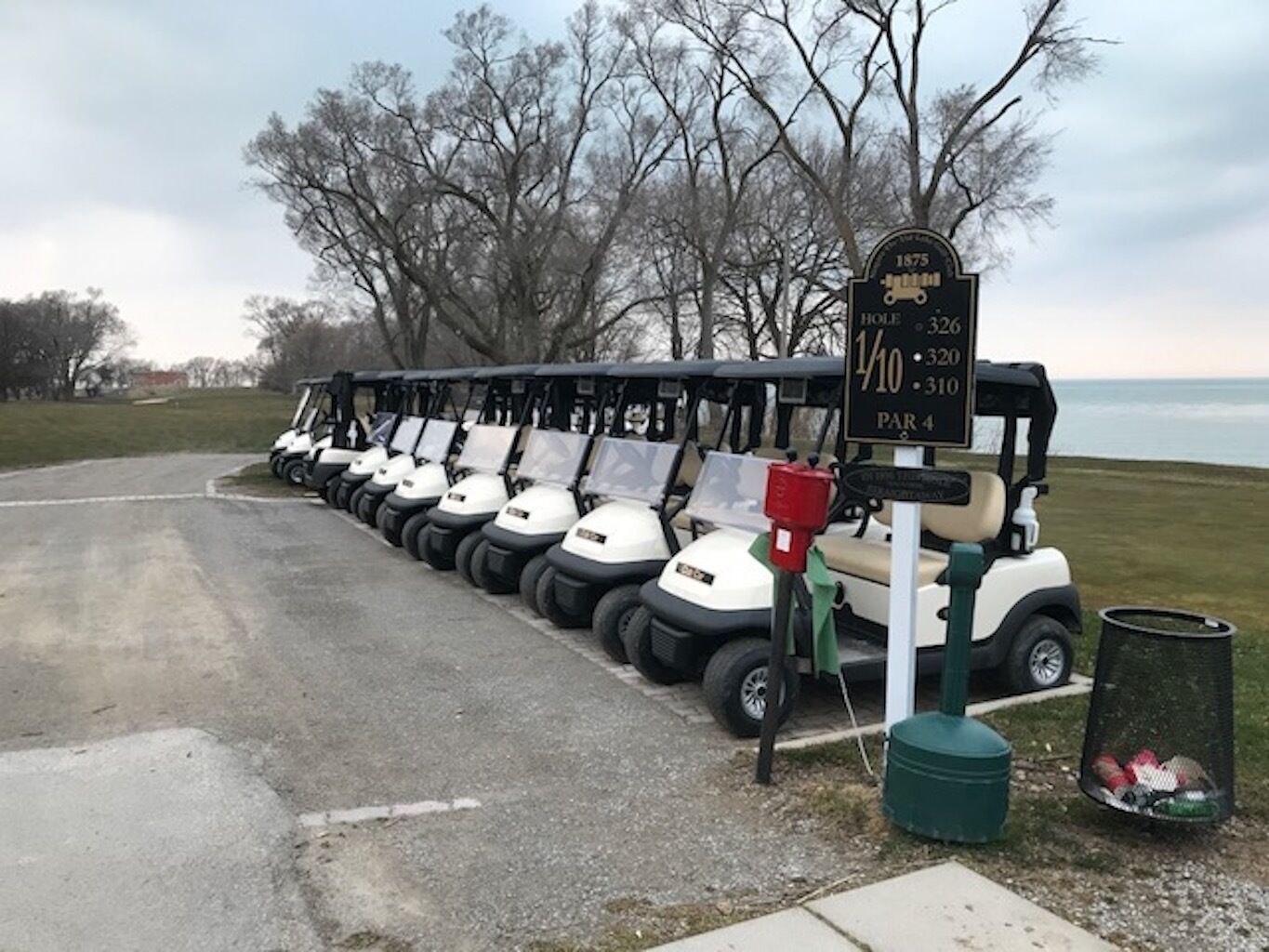 Filea di golf cart parcheggiata lungo una strada, con un cartello che indica il numero della buca e il par.