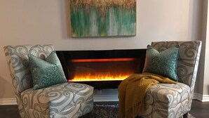 Deux fauteuils à motifs sont placés face à une cheminée, au-dessus de laquelle on peut voir un tableau décoratif.