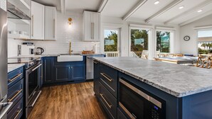 Una cucina moderna con mobili bianchi e blu scuro, un piano di lavoro in marmo e un pavimento in legno.