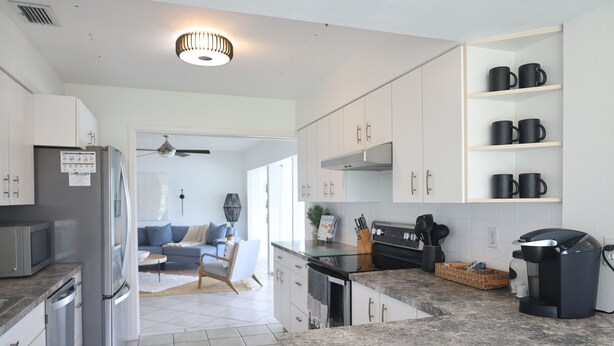 Eine moderne Küche mit weißen Schränken, einem Einbauofen, einer Kaffeemaschine und einem Essbereich mit einer Couch und einem Deckenventilator.