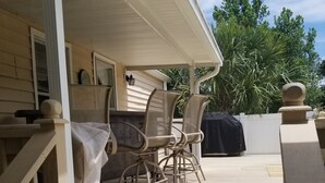 A covered outdoor patio with a wooden deck, a grill, and two chairs.