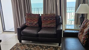 Un salón con sofá, alfombra estampada y vista al mar a través de grandes ventanales.