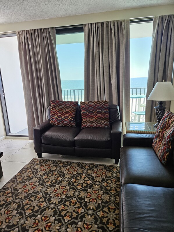 Un salón con sofá, alfombra estampada y vista al mar a través de grandes ventanales.