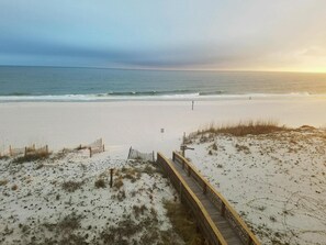 A beach with a wooden boardwalk leading to the water, sandy dunes, and a clear view of the ocean.